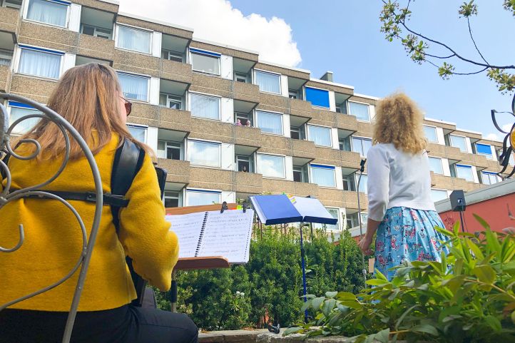 Zwei Frauen spielen vor einem Gebäude Musik für die Bewohner