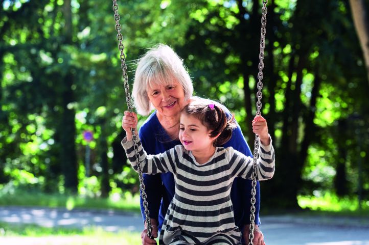 Frau schubst ein Mädchen an der Schaukel an. 