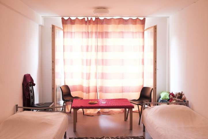 In einem leeren kleinen Zimmer stehen ein Tisch mit Stühlen und zwei Betten
