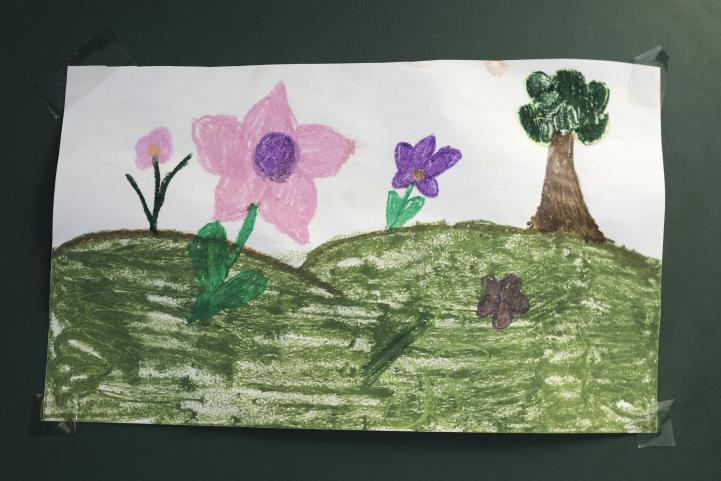 Eine Kinderzeichnung mit einer grünen Wiese, Blumen und einem Baum 