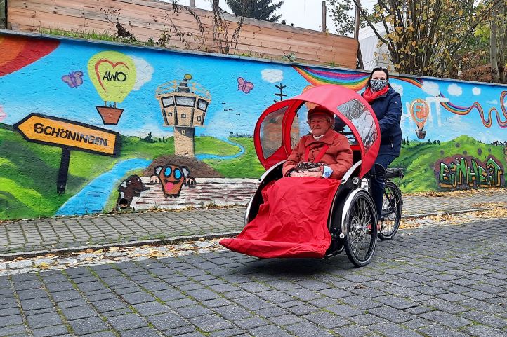 Zwei Frauen mit einem Riksha fahren an einer bunten Mauer entlang